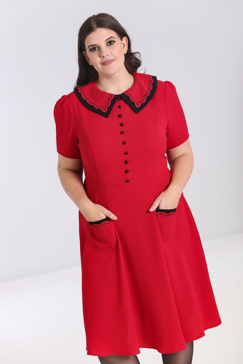 Plus size brunette model with brown eyes standing with her hands in the front pockets of her red dress
