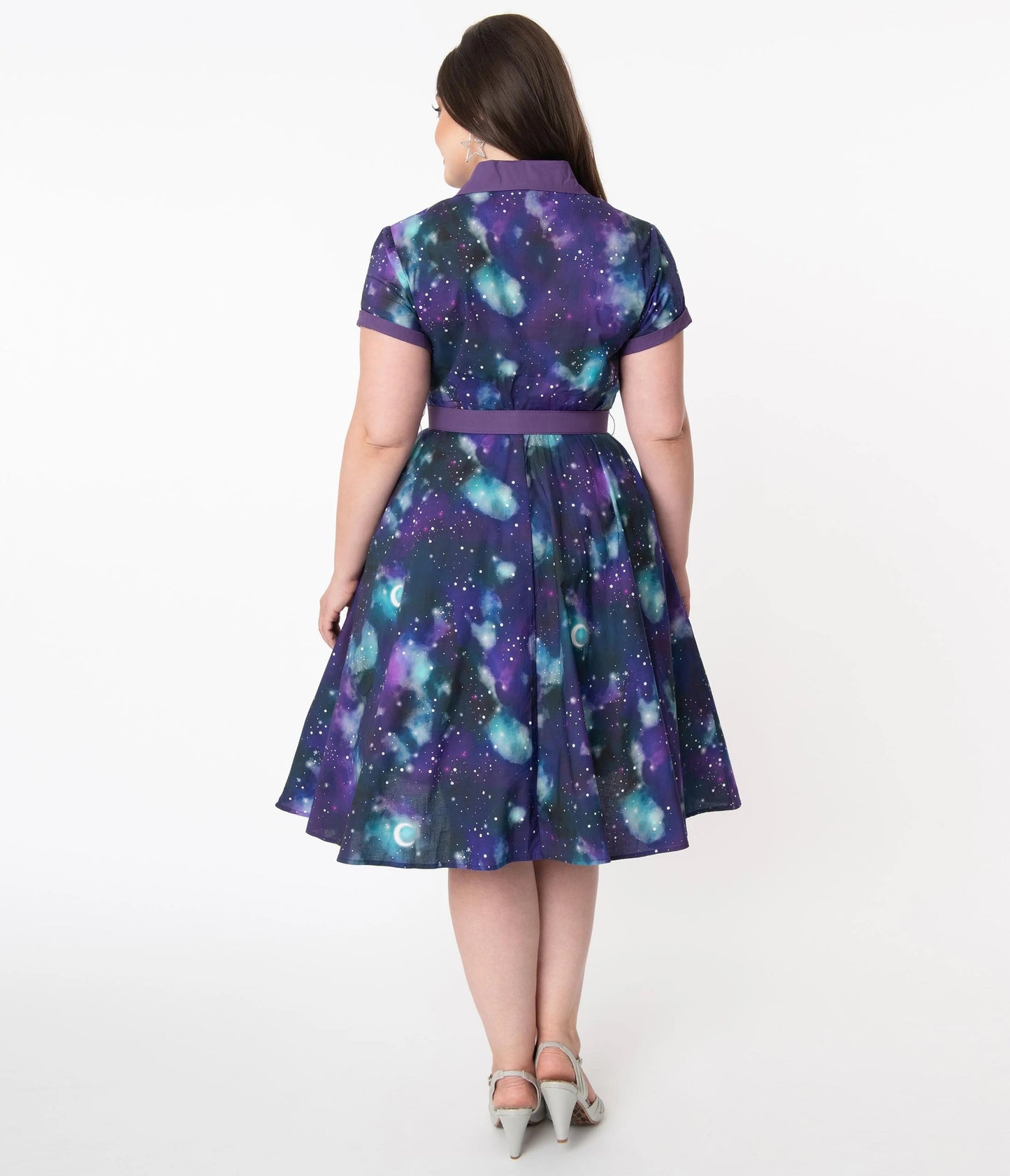View of the back of a brunette model wearing a purple galaxy/space print dress and silver glittery shoes with a white background