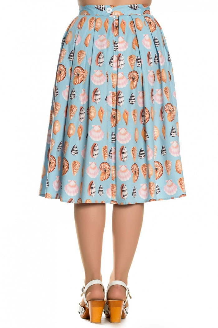 woman standing wearing heels and a light blue seashell print knee length skirt.
