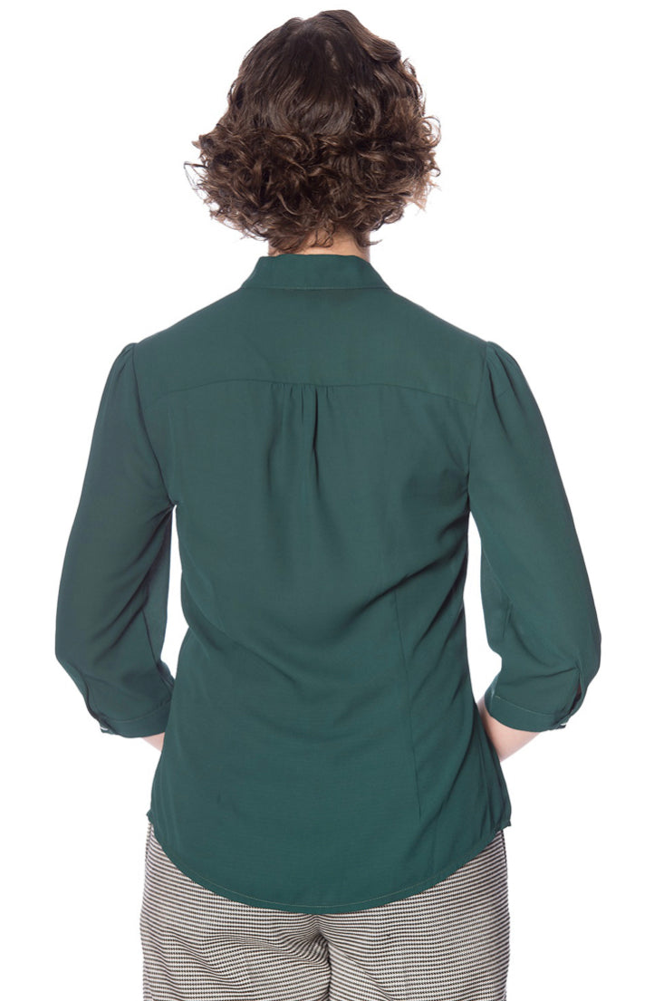 The Banned Retro 40s style pussybow blouse from the back untucked, paired with houndstooth trousers.