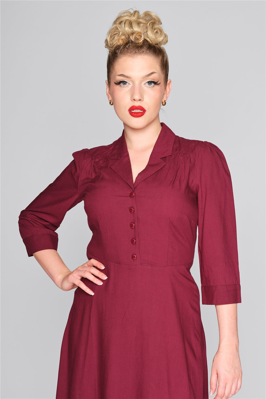 Woman wearing a burgundy 50s dress with a shirt collar and button front with a hand on her hip