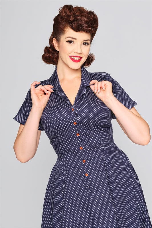 Happy, smiling woman holding the collar of her navy blue shirt dress.