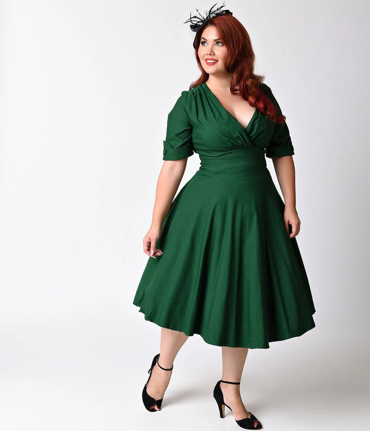 Beautifully dressed woman with long auburn hair standing wearing a fascinator, black high heels and an elegant deep green fit and flare swing dress