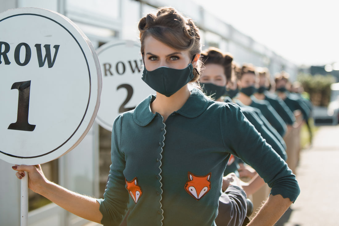 Brunette girl with victory rolls in her hair lines up with the other pit girls at Goodwood Racecourse ready for the race to begin