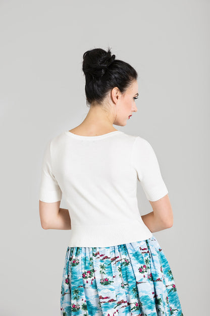 Dark haired woman looking to the right wearing a short sleeved ivory cardigan and blue 50s skirt