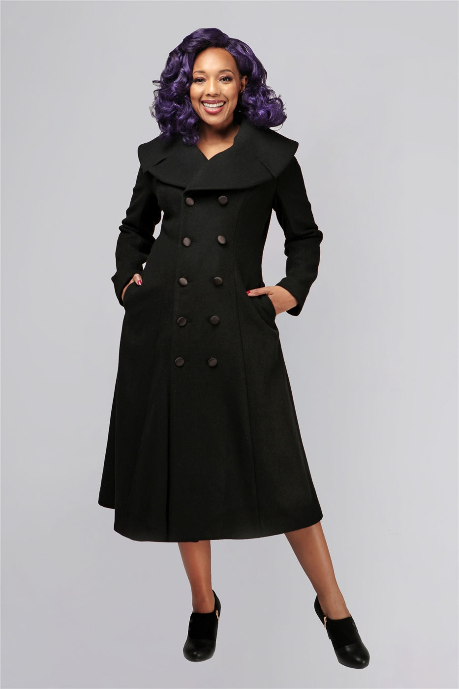 smiling model with curly purple hair standing with her hands in her coat pockets 