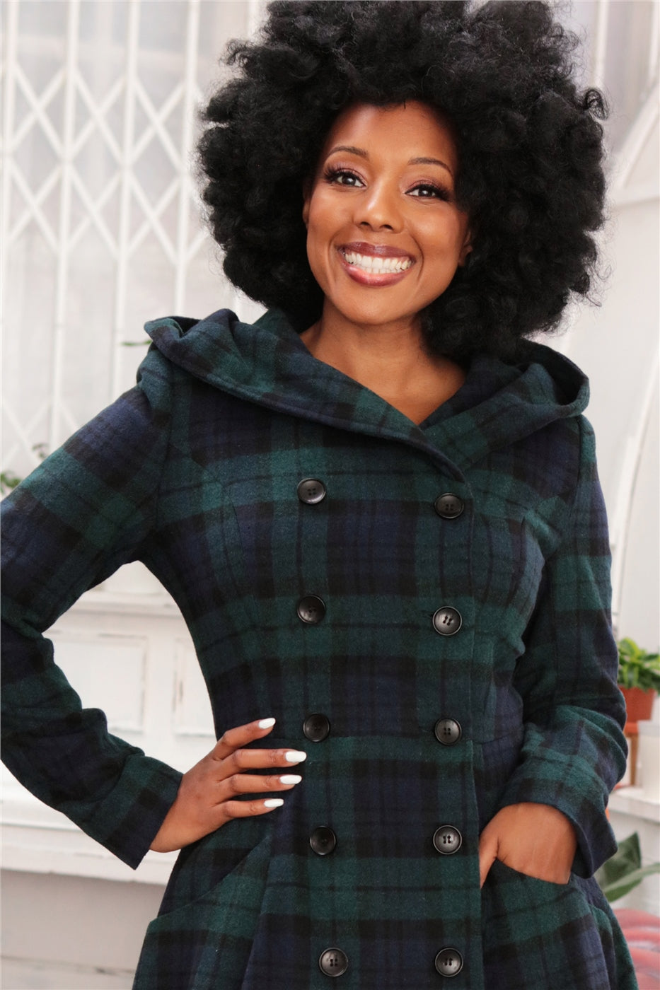 Happy, smiling woman with one hand on her hip wearing natural makeup and a warm winter tartan coat