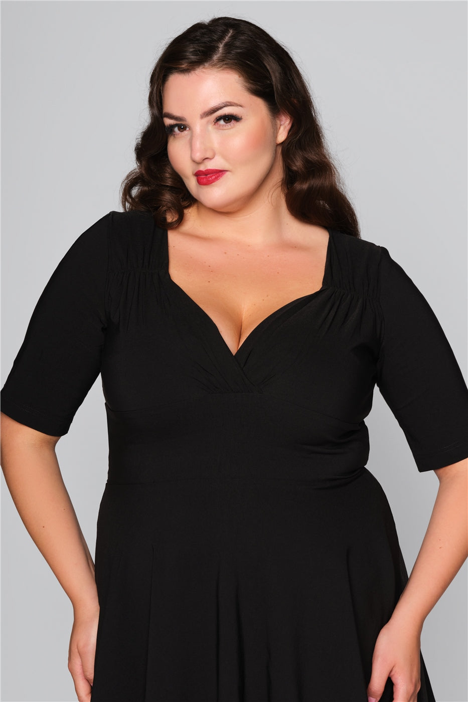 Pretty brunette vintage style model wearing a black dress with a flattering sweetheart neckline and three quarter length sleeves