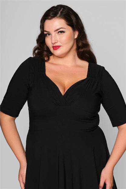 Pretty brunette vintage style model wearing a black dress with a flattering sweetheart neckline and three quarter length sleeves