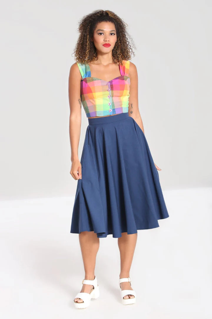 A pretty young lady standing with her arms by her sides wearing a rainbow check button front top and a navy blue swing skirt with white sandals