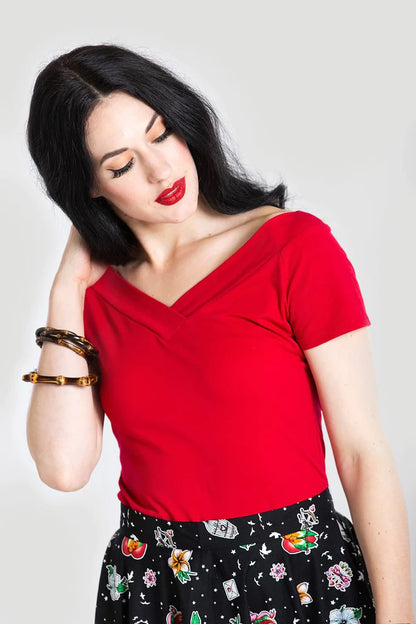 Petite woman with long black hair and red lipstick pushing her hair behind her shoulder. She is wearing a Red plain T-shirt style Alex top and a black skirt