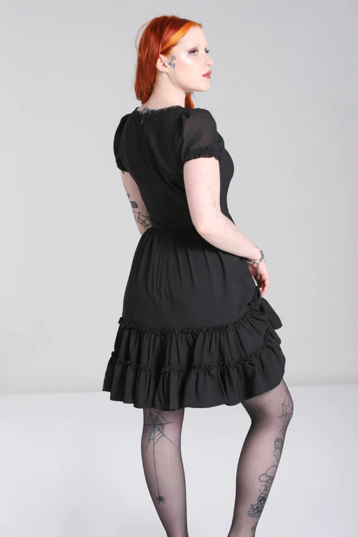Tattooed girl with bright orange hair wearing the black Annette dress facing away from camera with one hand on her hip and her weight on her left leg
