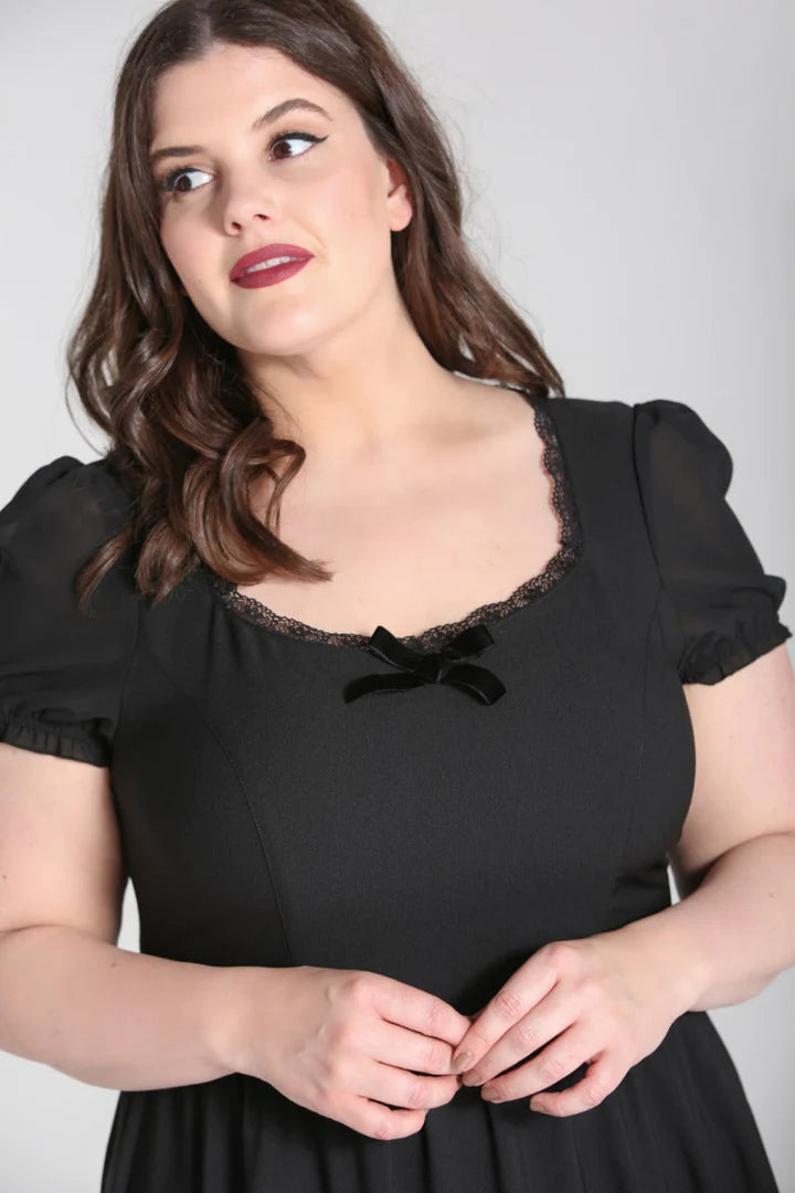 Curvy woman with dark hair and red lipstick stands with her hands at waist level wearing a black dress