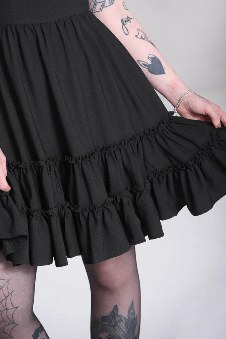 A girl with tattoos shows off the details at waist level of the black dress she is wearing