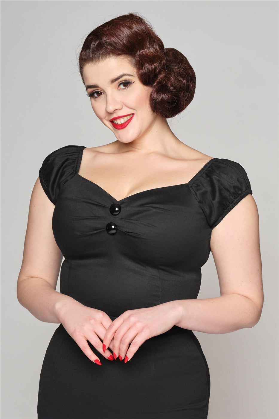 Brunette woman with red lipstick and nails wearing the Dolores off the shoulder sleeve top and a black pencil skirt