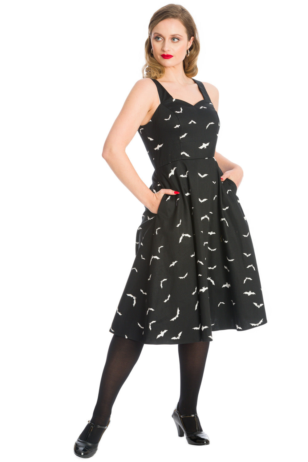 Blonde woman standing gracefully in a stylish black swing dress adorned with a captivating all-over white bat print and her hands in the side pockets