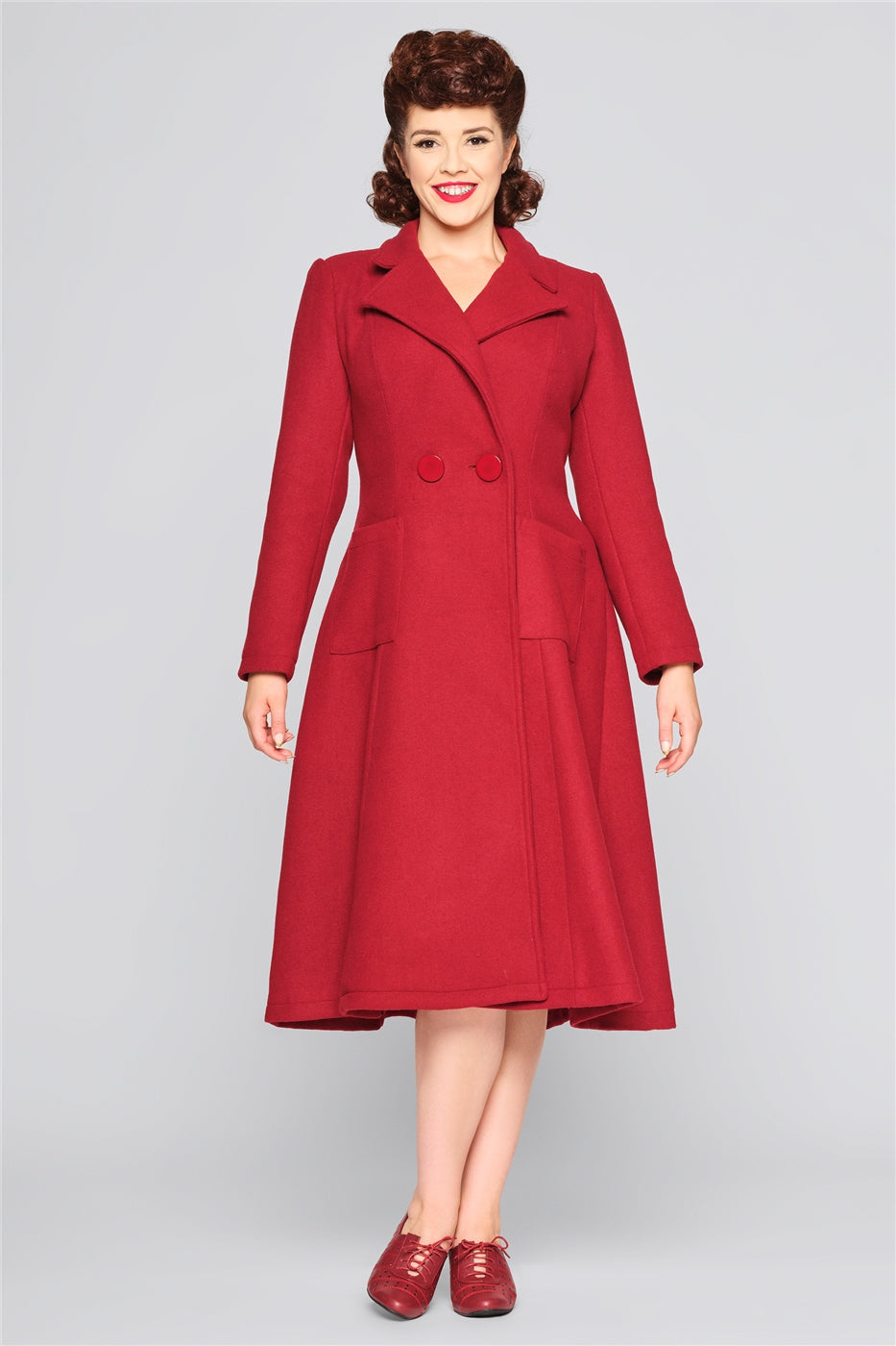 Smiling vintage model with brown hair in a classy updo wearing a burgundy winter coat with a fitted waist and flared skirt