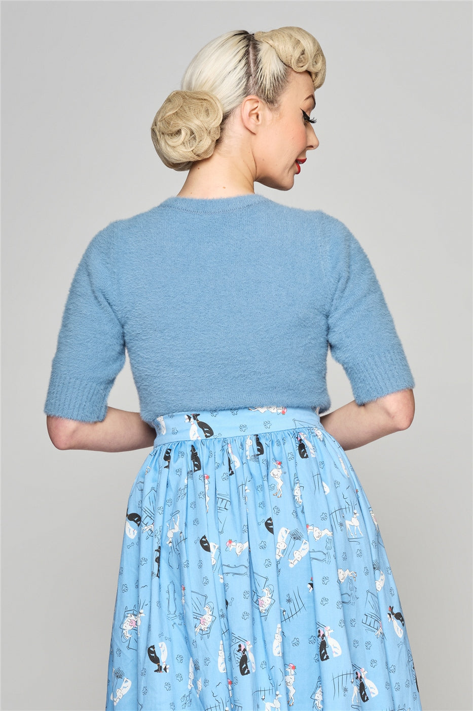 Blonde woman with vintage makeup facing away from the camera wearing a blue fluffy Chrissie top and blue poodle skirt
