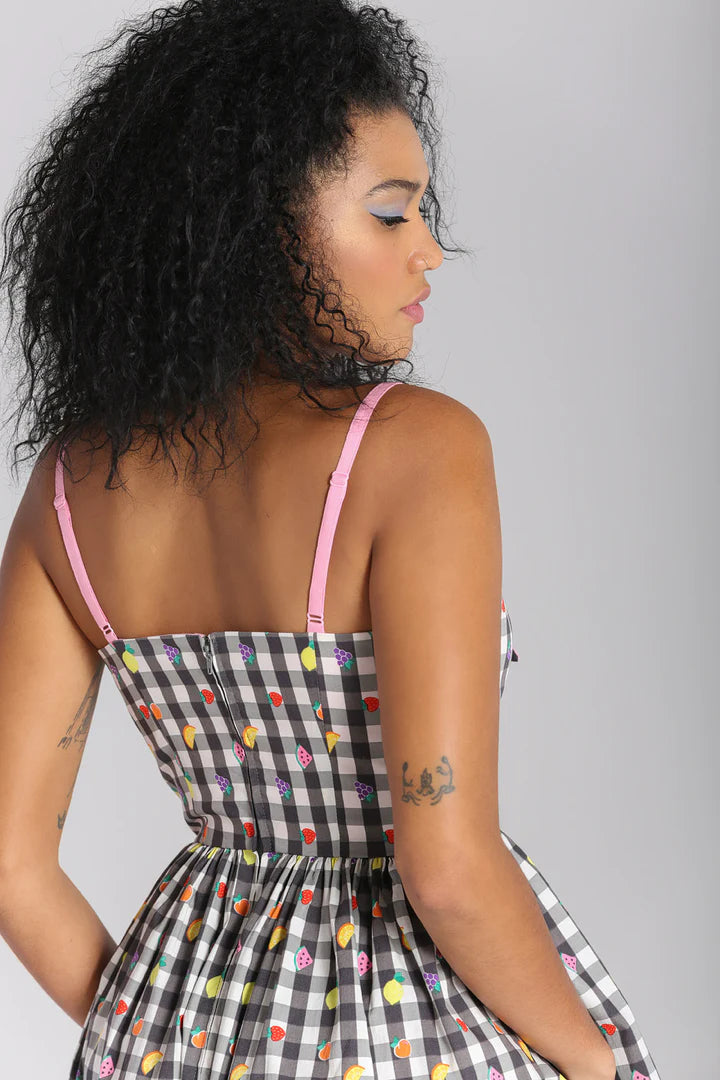 Young woman facing away from the camera looking down wearing the Fruity Lou dress by Hell Bunny. The dress features pink adjustable straps  and pockets! 