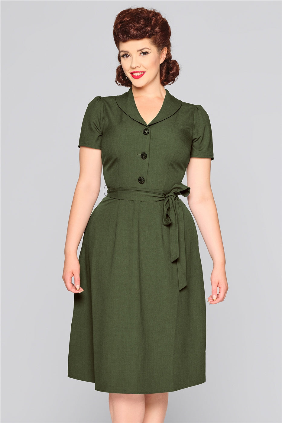 Pretty vintage lady standing with her arms by her sides smiling, wearing a classic 40s style dress with button front  and short sleeves.