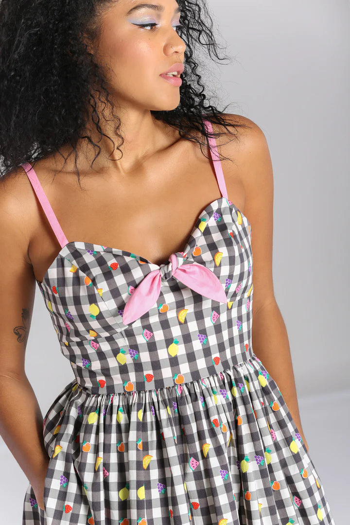 Young woman with dark curly hair wearing purple and pink eyeshadow and the Fruity Lou gingham and multicoloured fruit print dress with little watermelon slices, citrus fruits, strawberries and grapes print all over.