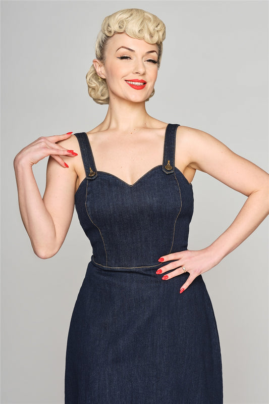 Happily smiling blonde woman with orange-red lipstick and red painted nails wearing a dark blue denim pinafore dress. 