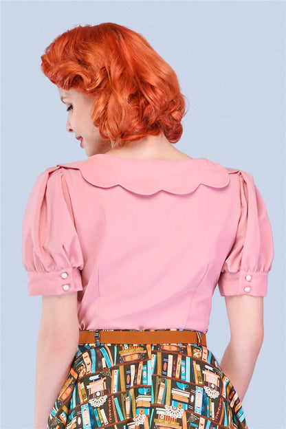 elegant red haired woman facing away from the camera wearing a pink blouse with a pretty scalloped collar and short puff sleeves with small button detail 