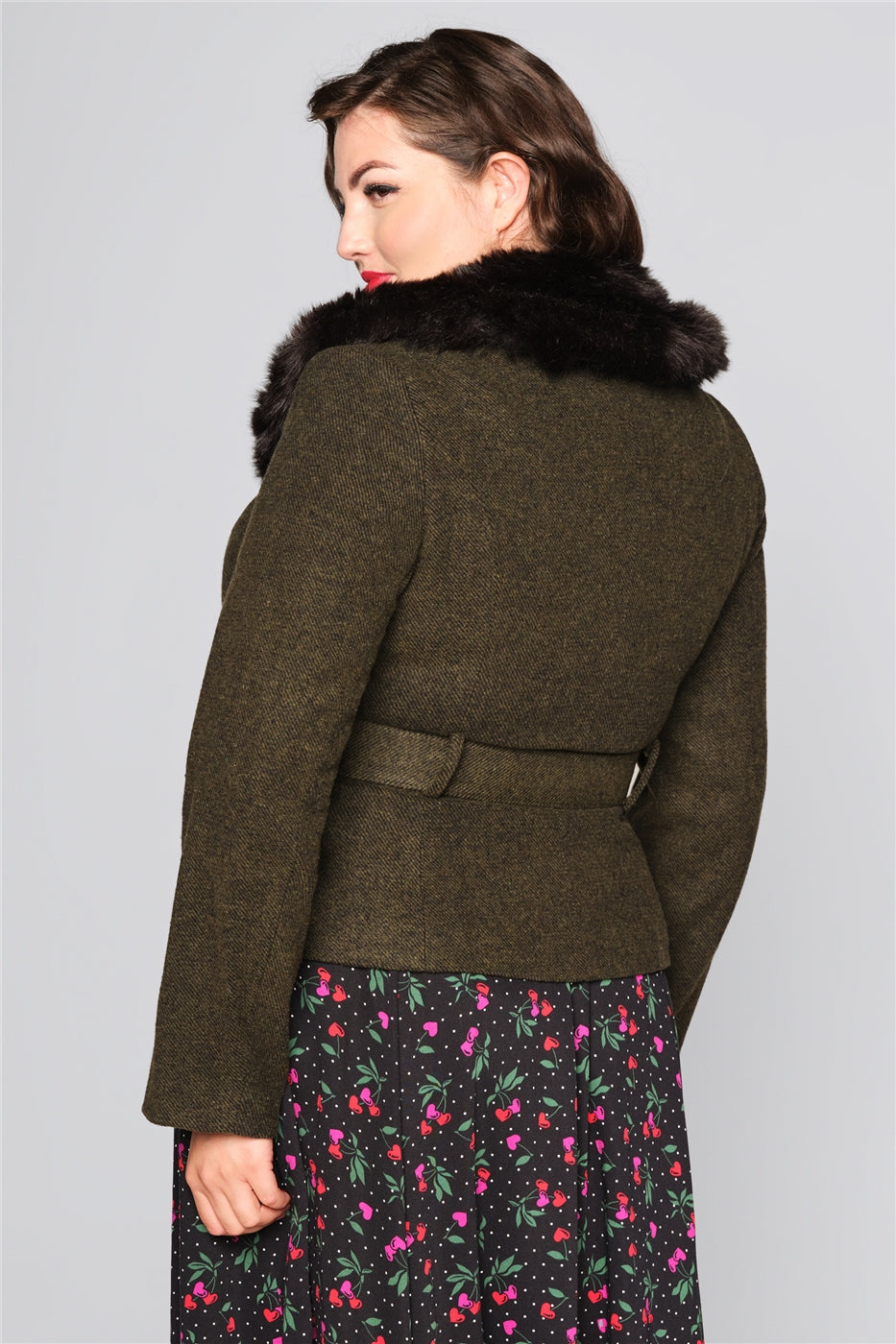 Plus size model with brown hair and 50s makeup wearing a fitted green jacket with black faux fur trim collar