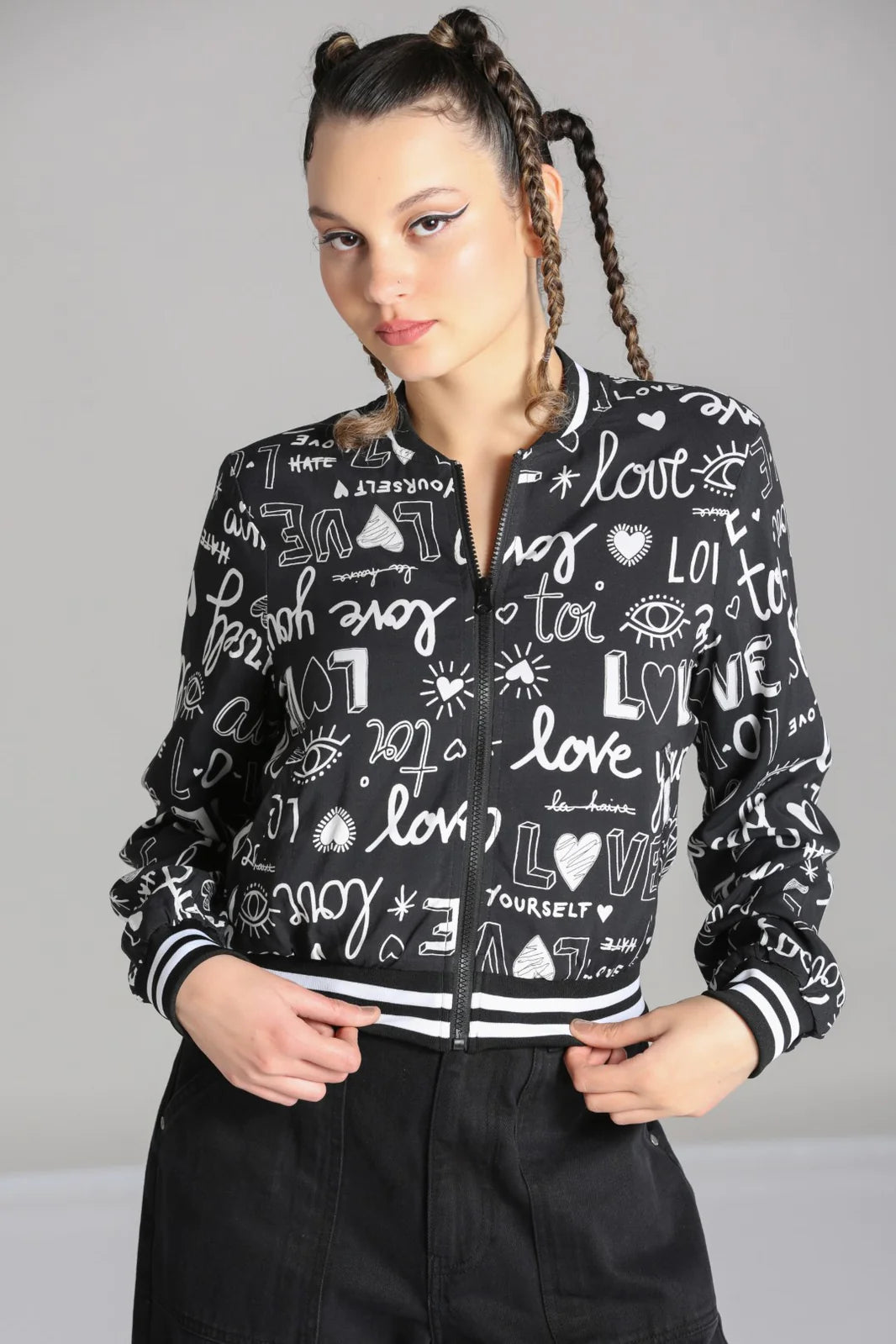 Young lady with plaited hair standing holding the front of her zip-front Love Yourself jacket 