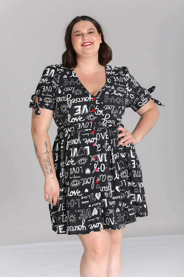 Young woman with a radiant smile standing with one hand on her hip. she is wearing the Love Yourself Mini Dress by Hell Bunny which drops to a few inches above the knee.