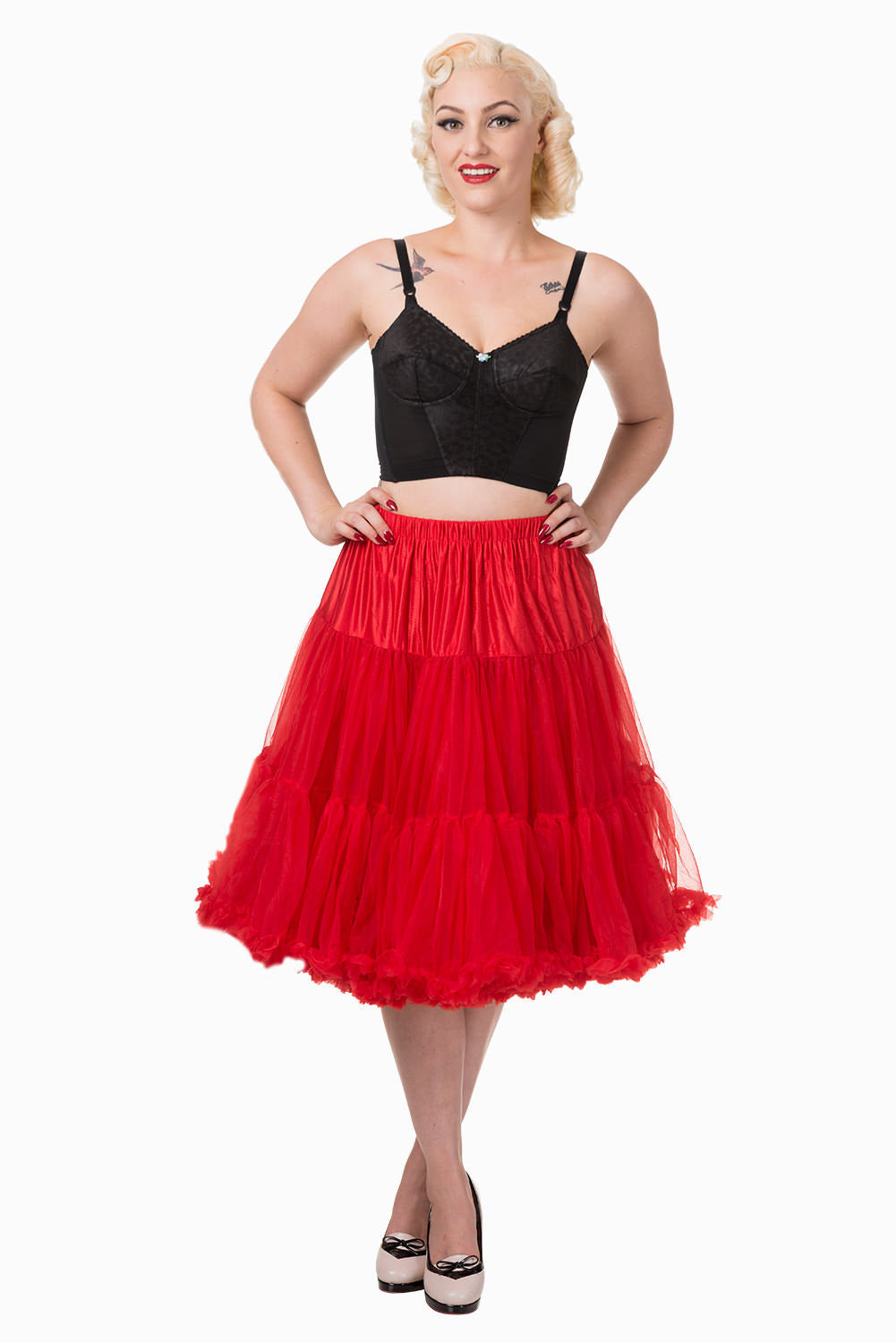 Blonde woman wearing red lipstick standing with her hands on her hips wearing a classic 50s red petticoat and high heels