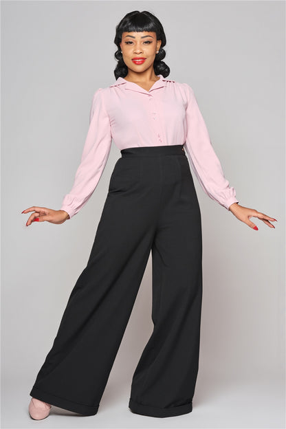Tall, elegant woman with classic 40s makeup wearing wide leg swing trousers, a button front long sleeved pink blouse and pink pumps.