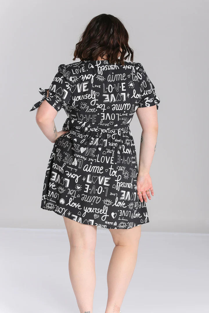 Curvy plus size woman with beautiful brown short hair standing facing away from the camera with one hand on her hips. She is wearing the Hell Bunny Love Yourself Mini Dress