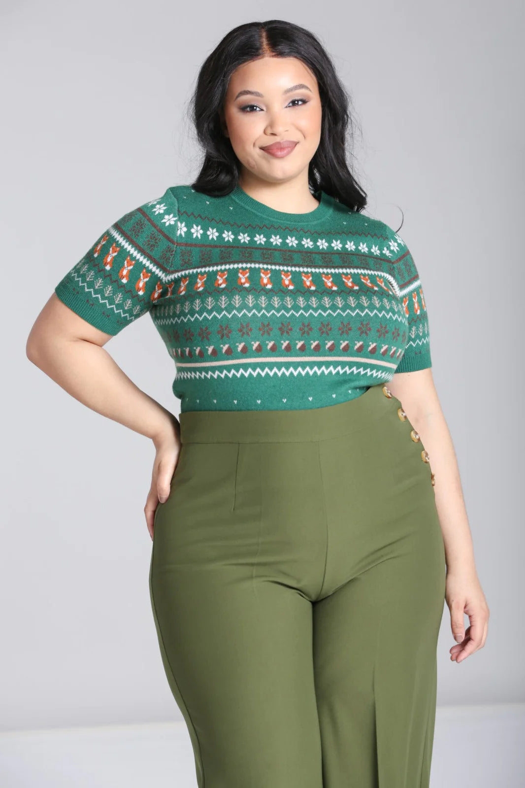 Smiling plus size woman wearing a green knitted Fair Isle style jumper with fox motif and high waisted green swing trousers