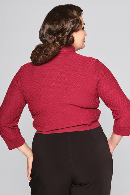 Curvy brunette model facing away with her hands in her pockets wearing the lattice knitted jumper and high waisted black trousers