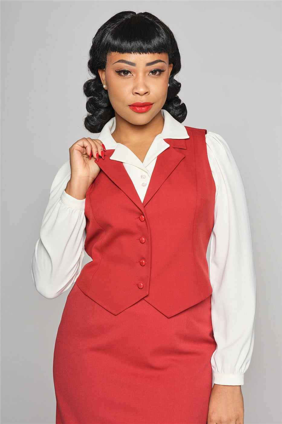 Dark haired woman with dark hair, brown eyes and vintage style makeup wearing the Professor red waist coat over the ivory Pepper blouse and a red pencil skirt