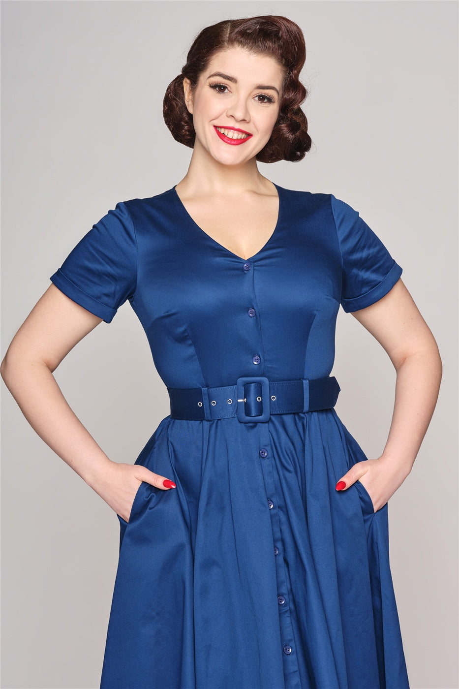 Elegant woman with neat, styled up-do wearing the Shana navy blue swing dress standing with her hands in her pockets