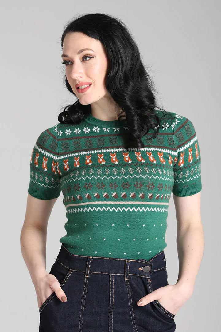 Dark haired woman smiling and standing with her hands in the pockets of her jeans wearing the Vixey Green jumper.