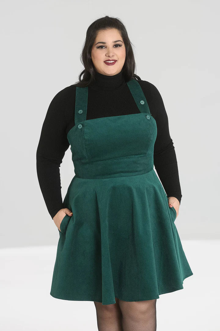 Happy woman with a radiant smile standing with her hands in the pockets of her pinafore dress