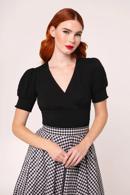 Woman wearing a black top and checkered skirt against a plain background