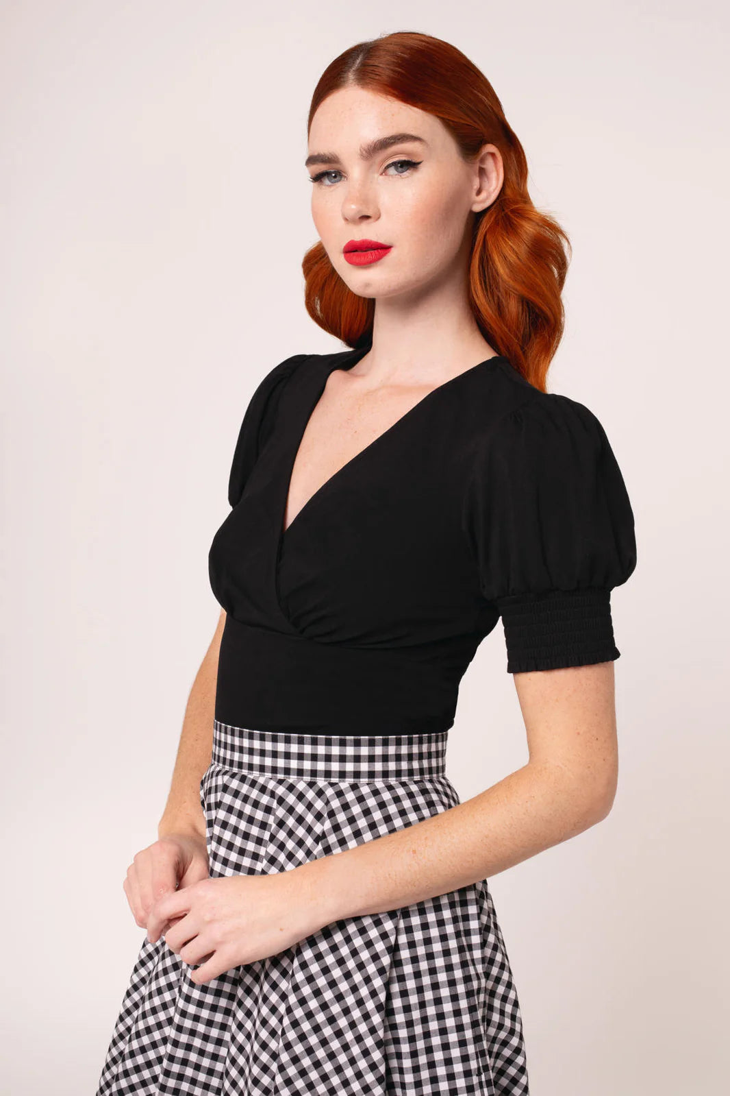 Woman wearing a black top and checkered skirt against a plain background