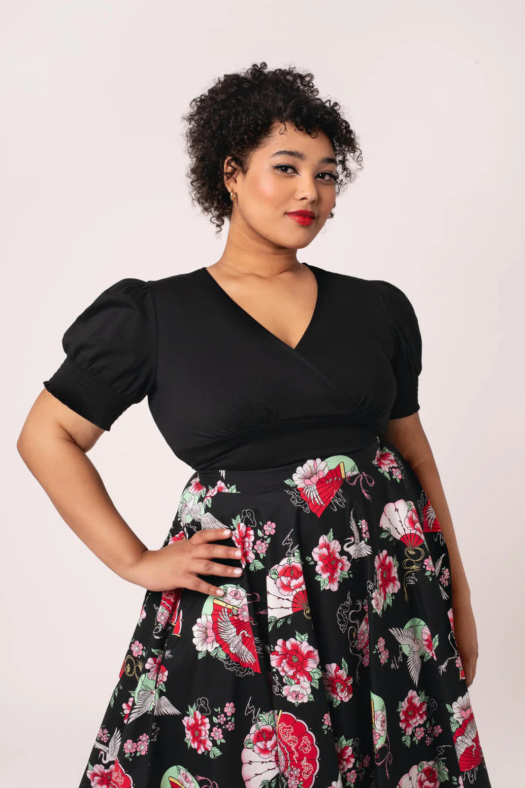 Woman wearing a black top and floral skirt against a white background