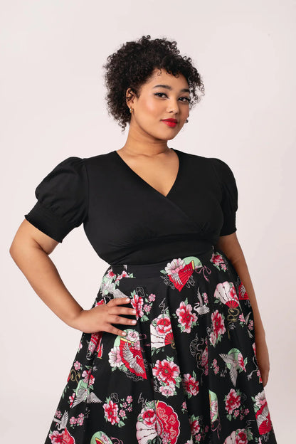 Woman wearing a black top and floral skirt against a white background