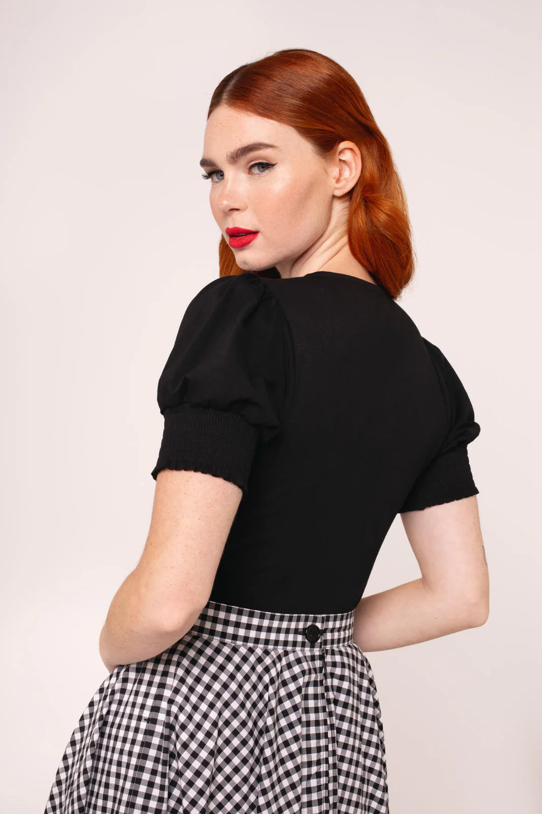 Woman wearing a black top with puff sleeves and a checked skirt on a light background