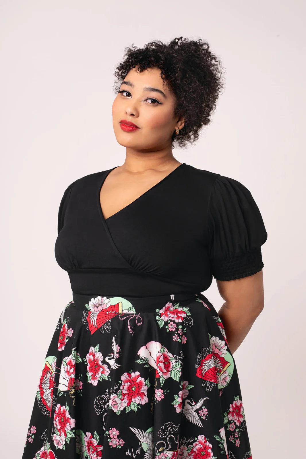 Woman wearing a black wrap-front top with floral skirt against a white background