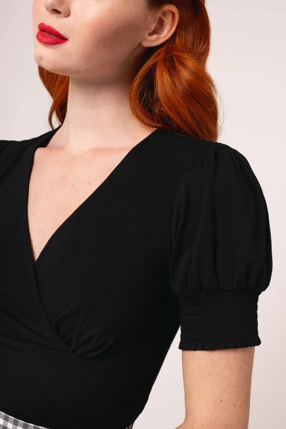 Woman wearing a black top with puffed sleeves against a plain background