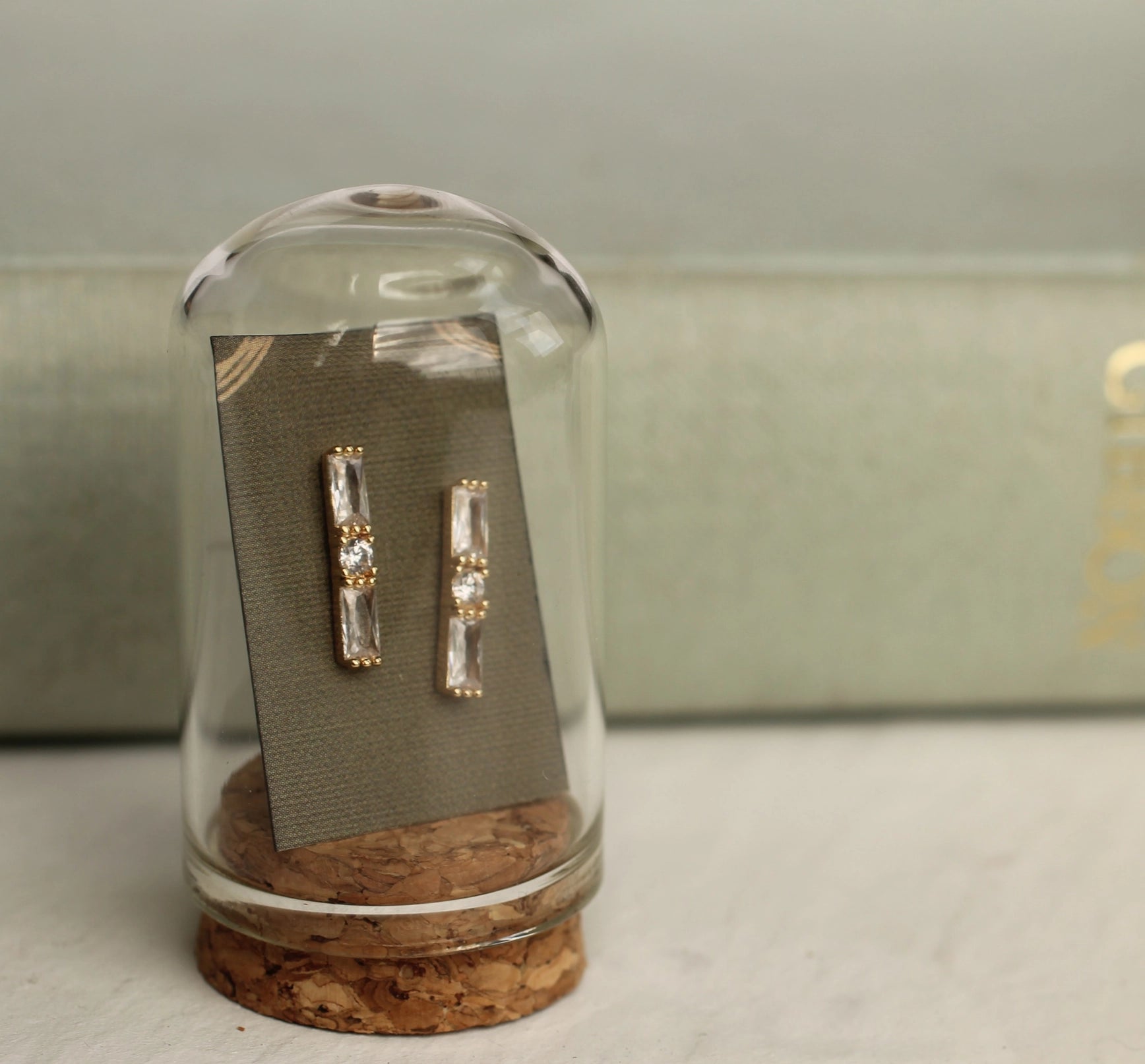 Gold and crystal earrings inside a glass dome on a light gray surface.