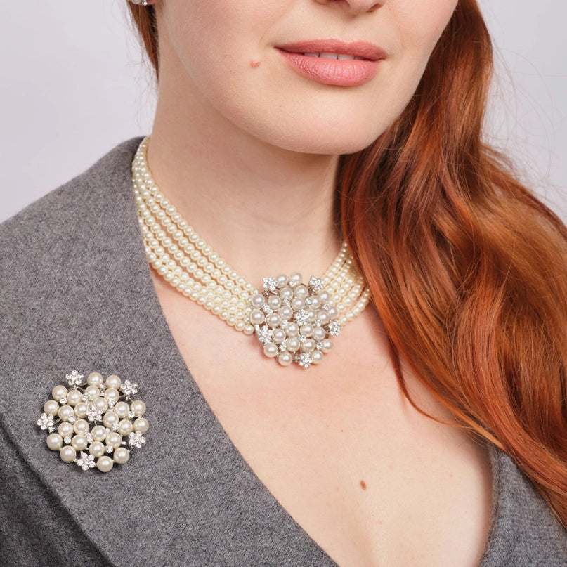 Smiling woman wearing a grey jacket adorned with a pearl and diamante brooch on the lapel, paired with an Audrey Hepburn-inspired pearl and diamante necklace from the Hepburn collection, designed to complement the matching clip-on earrings.