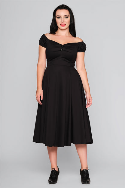Dark haired smiling woman wearing a 50s style mid length off the shoulder dress