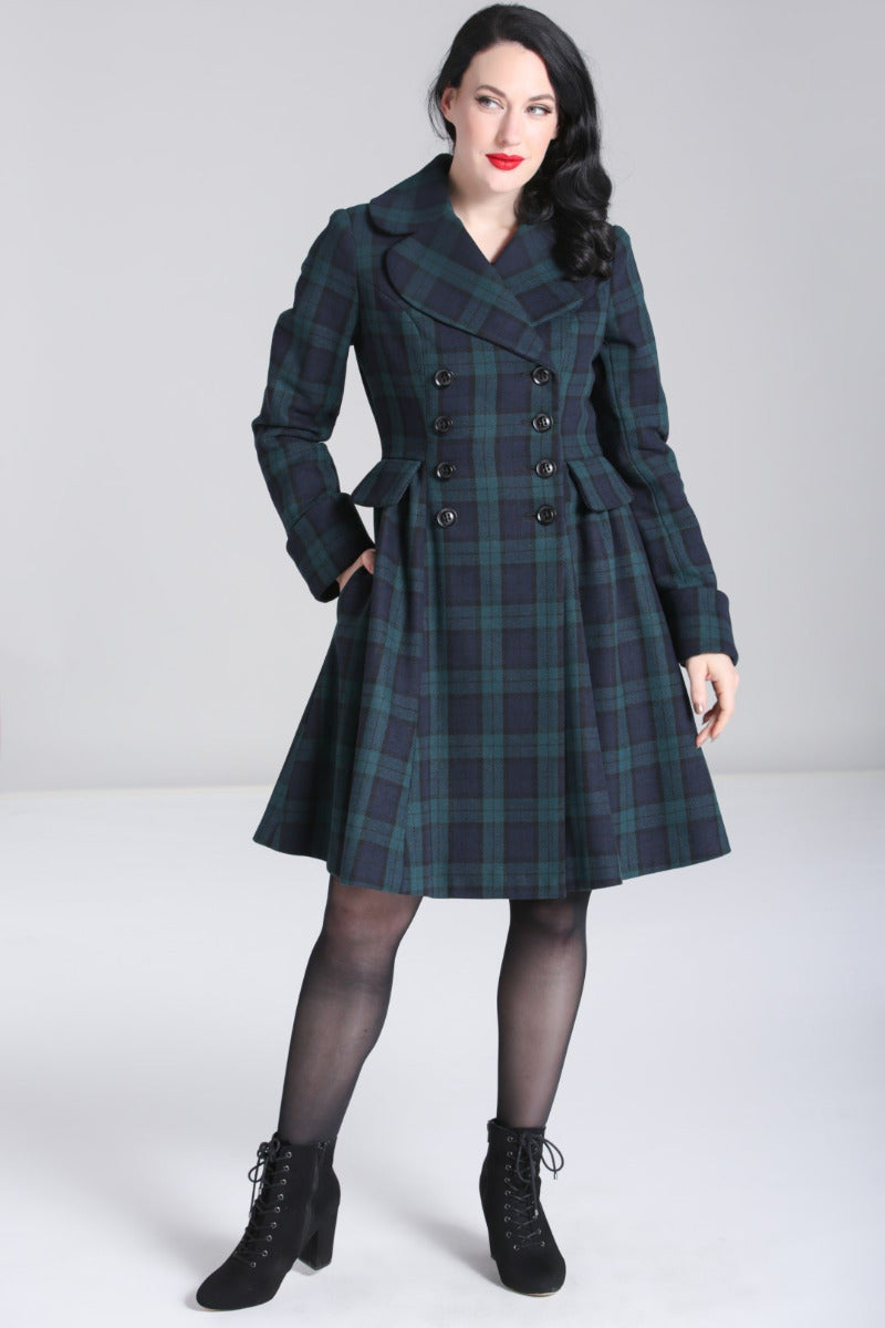 Dark haired woman wearing 50s style makeup standing with one hand in her coat pocket wearing black lace up boots